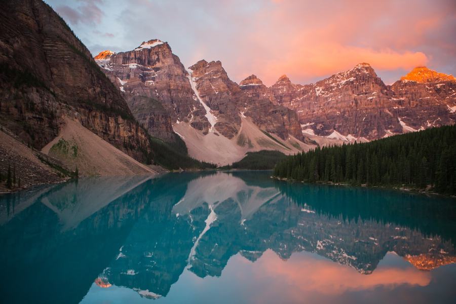 A turquoise mountain lake beneath peaks glowing pink at sunrise in the Canadian Rockies